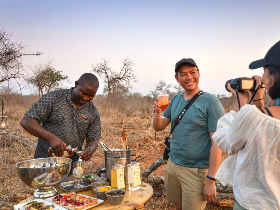 A group of people outdoors with a barbecue setup, including a metal bowl, bottles, and food.