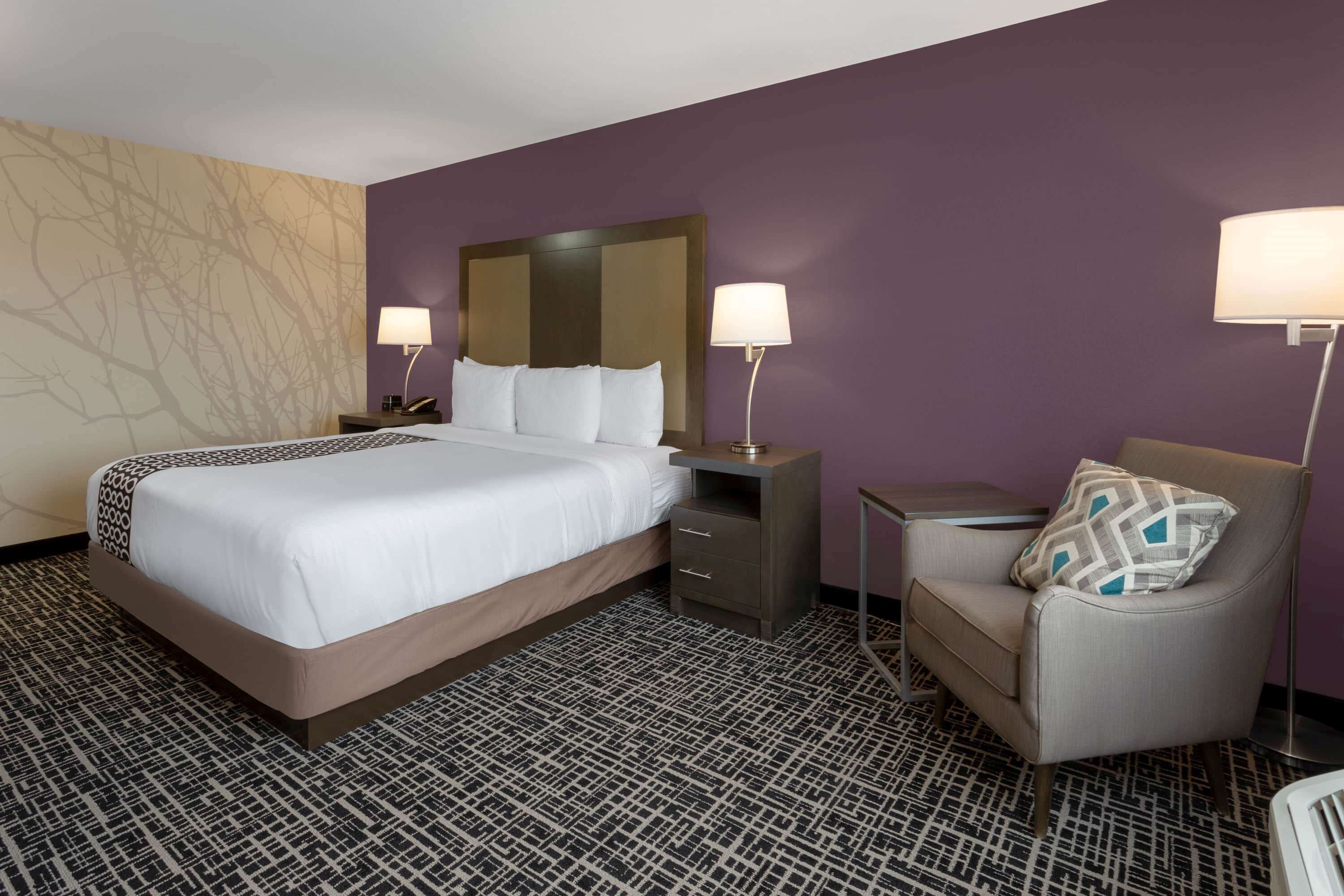 Een hotelkamer met een groot bed, twee nachtkastjes, een stoel en een kleine tafel.