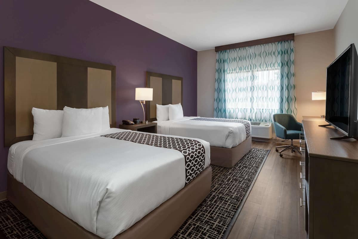 A hotel room with two beds, a desk, a chair, and a television.