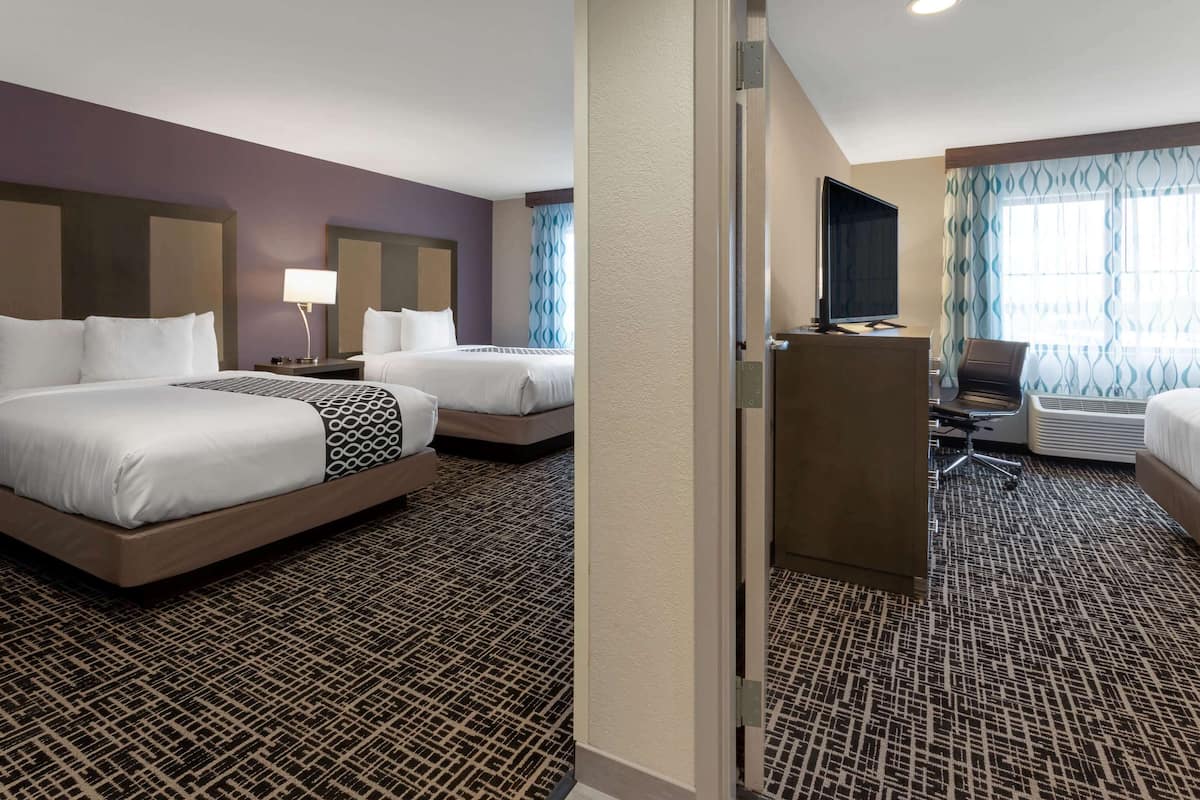 A hotel room with two beds, a desk, a TV, and a seating area.