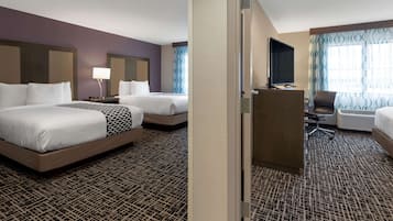 A hotel room with two beds, a desk, a TV, and a seating area.