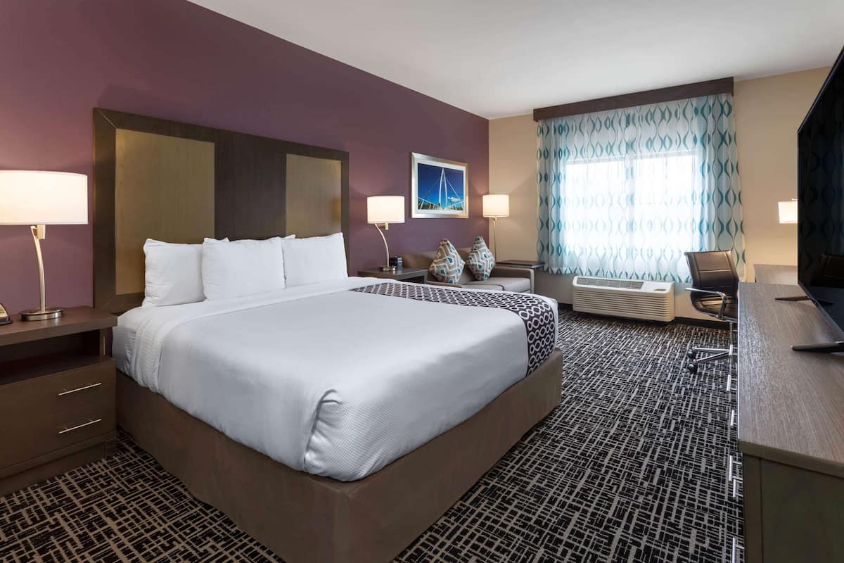 A hotel room with a large bed, two bedside tables, a desk, a chair, a TV, and a window with curtains.