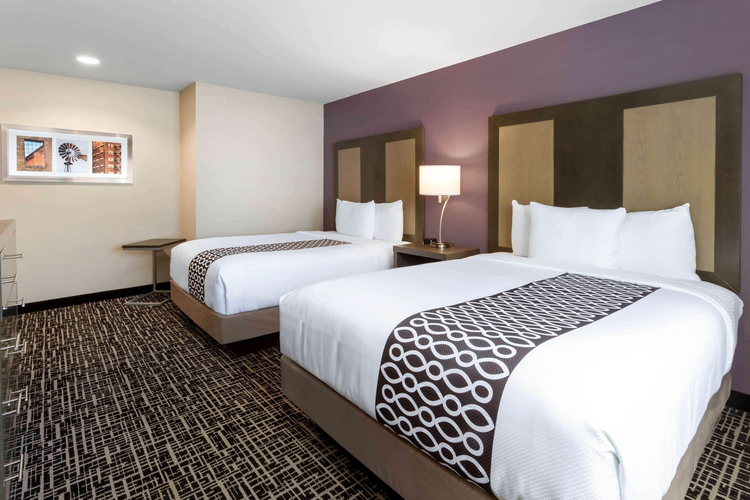 A hotel room with two beds, a nightstand with a lamp, and a patterned carpet.