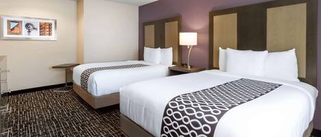 A hotel room with two beds, a nightstand with a lamp, and a patterned carpet.