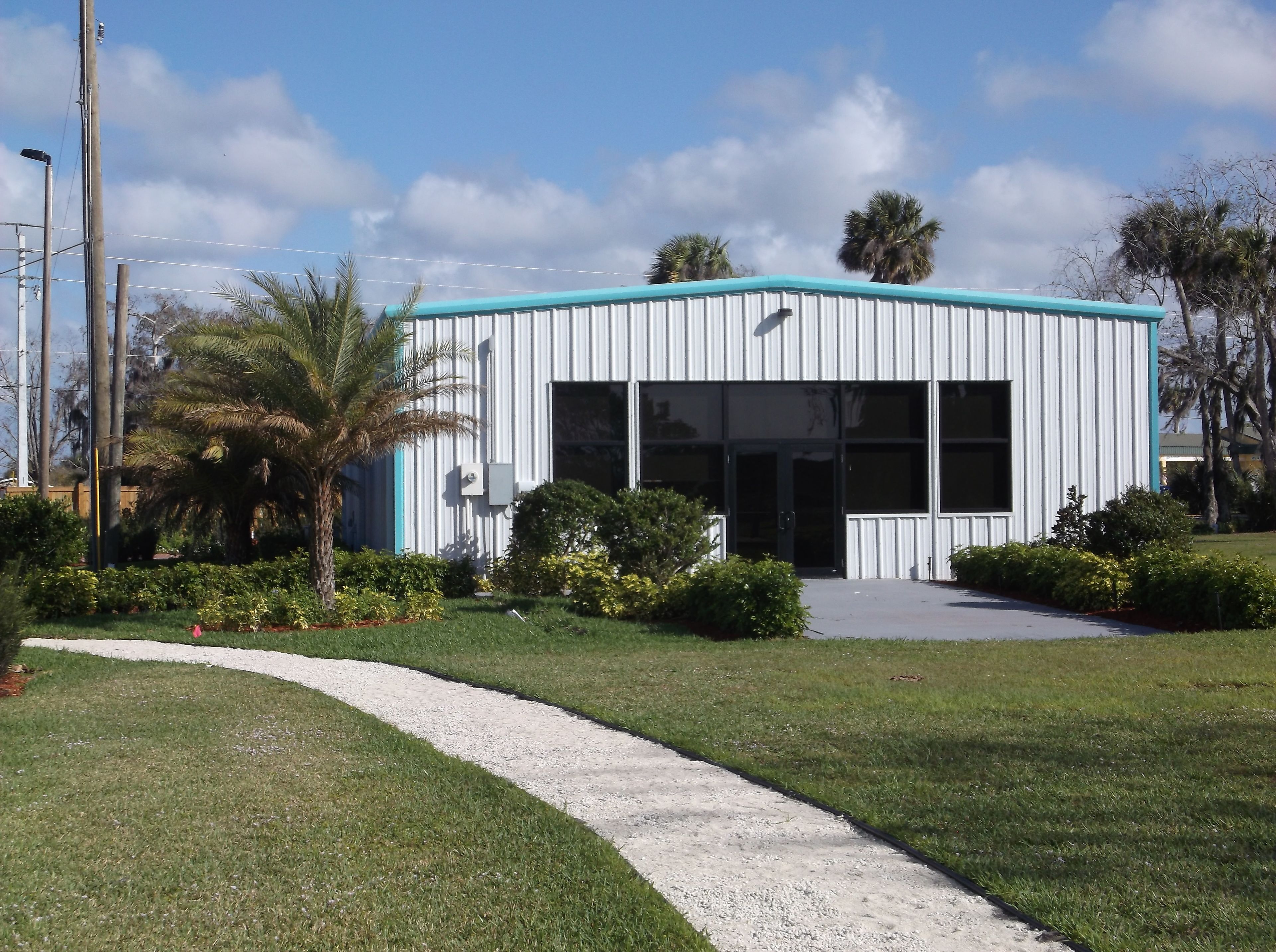 A modern building with a light blue roof, large windows, and a paved entrance area.