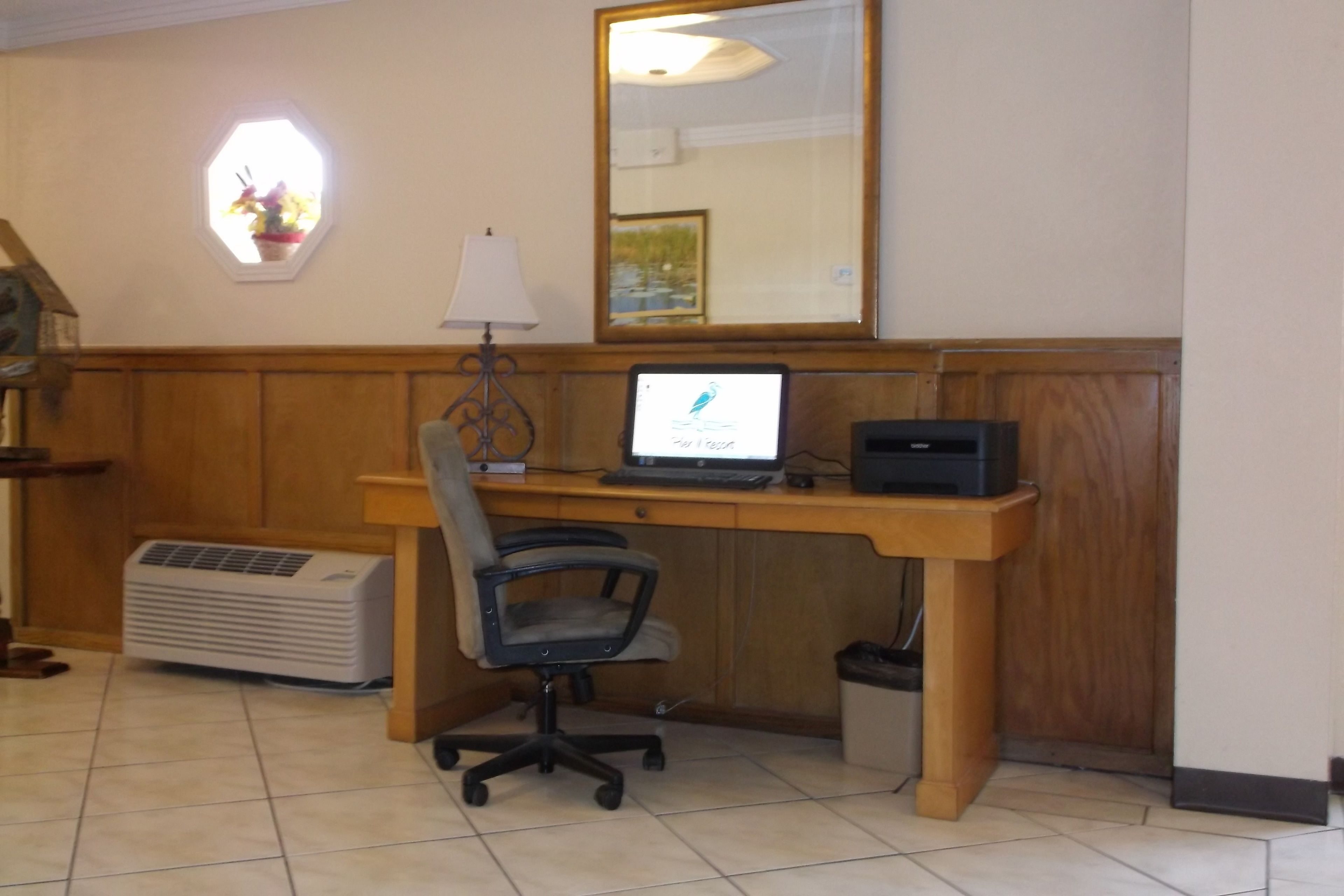 A room with a wooden desk, a computer, a chair, an air conditioner, a lamp, and a window with flowers.