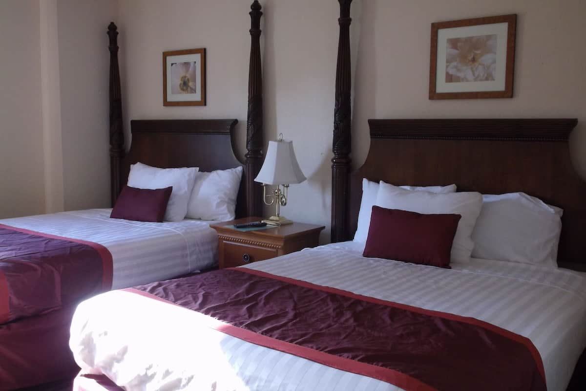 Two double beds with wooden headboards, a nightstand with a lamp, and framed pictures on the wall.