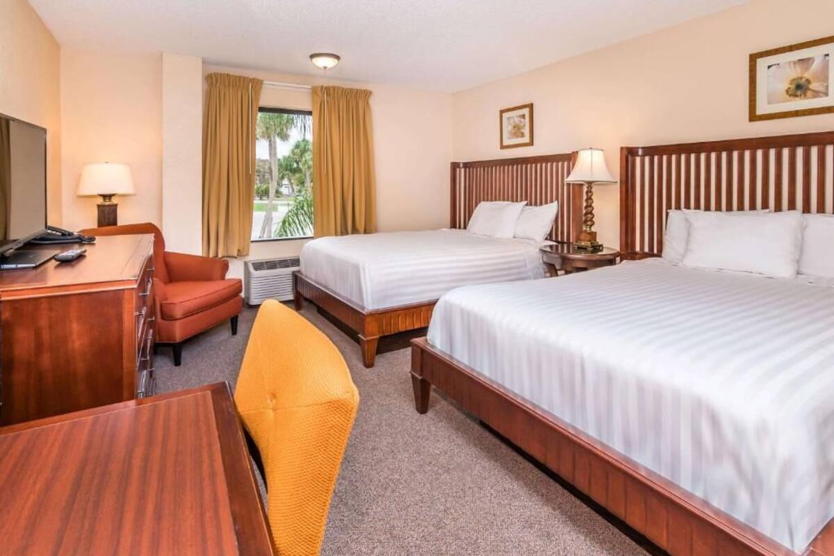 A hotel room with two beds, a desk, a chair, a TV, and a window with curtains.