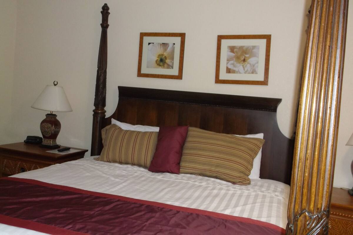 A neatly made bed with a wooden headboard, a bedside table with a lamp, and two framed pictures on the wall.
