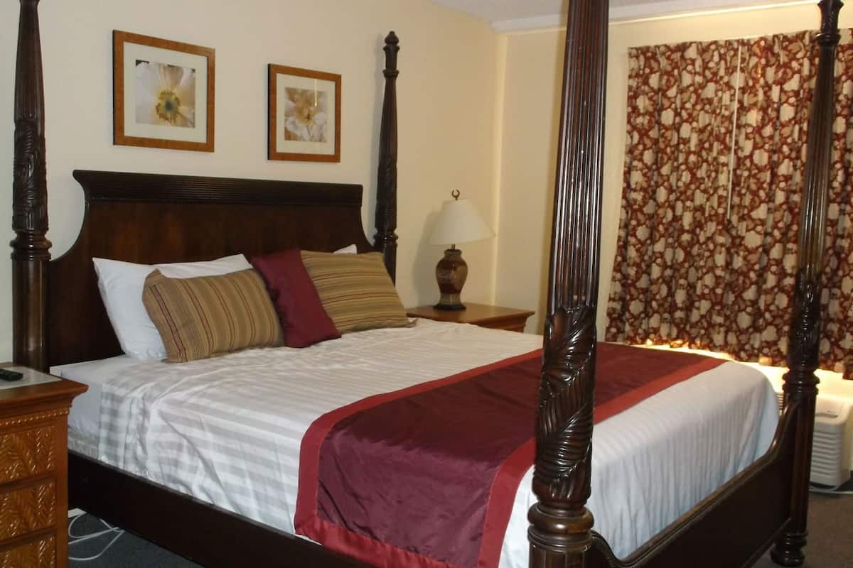 A four-poster bed with a wooden headboard, white bedding, and a red throw blanket. There are two framed pictures on the wall above the bed.