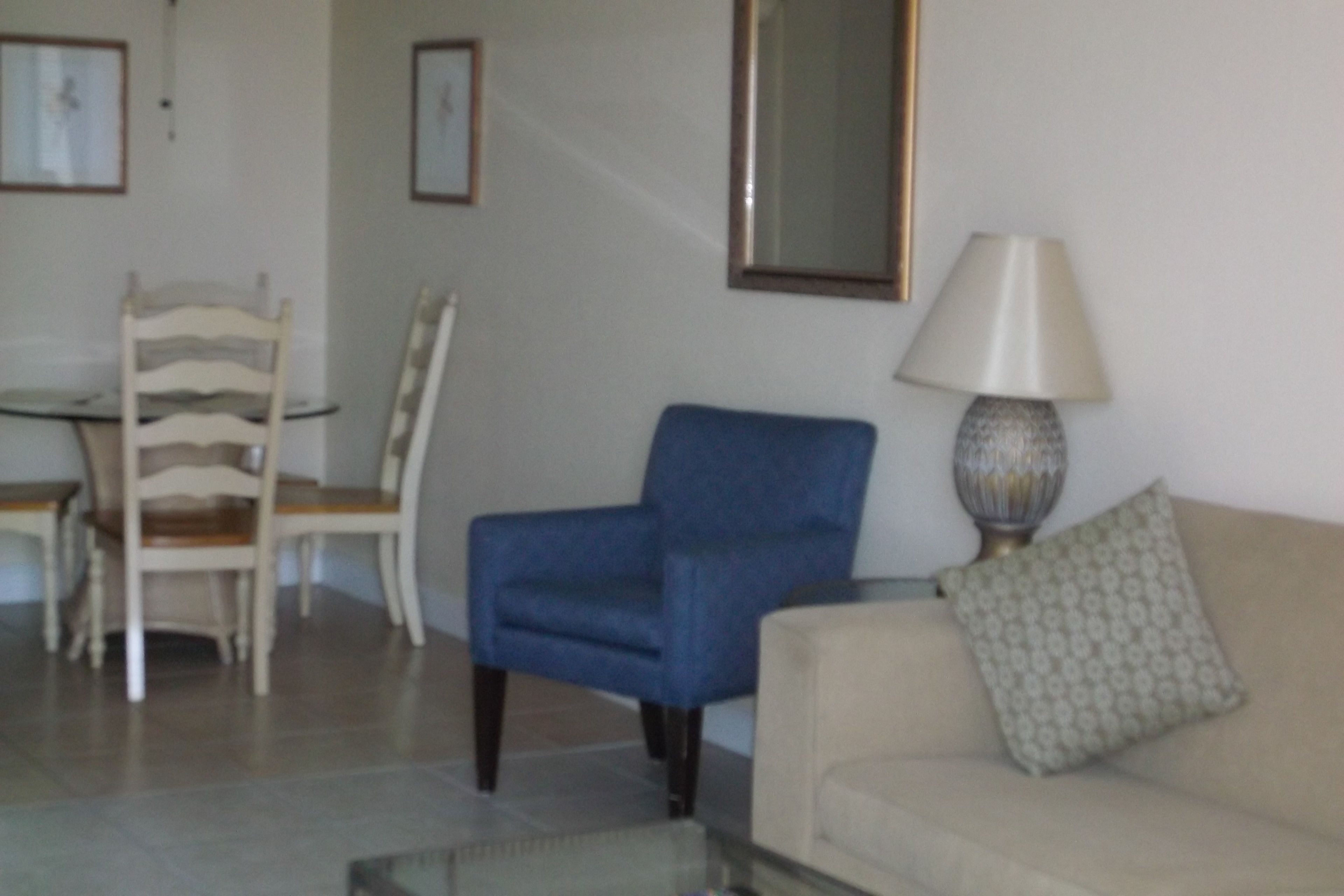 A living room with a beige sofa, a blue armchair, a glass coffee table, and a lamp.