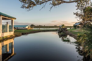 A tranquil pond with a gazebo, a small building with a green roof, and a distant house.