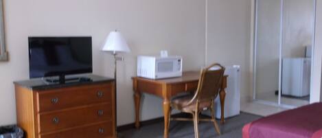 A hotel room with a wooden dresser, a television, a microwave, a chair, and two beds.