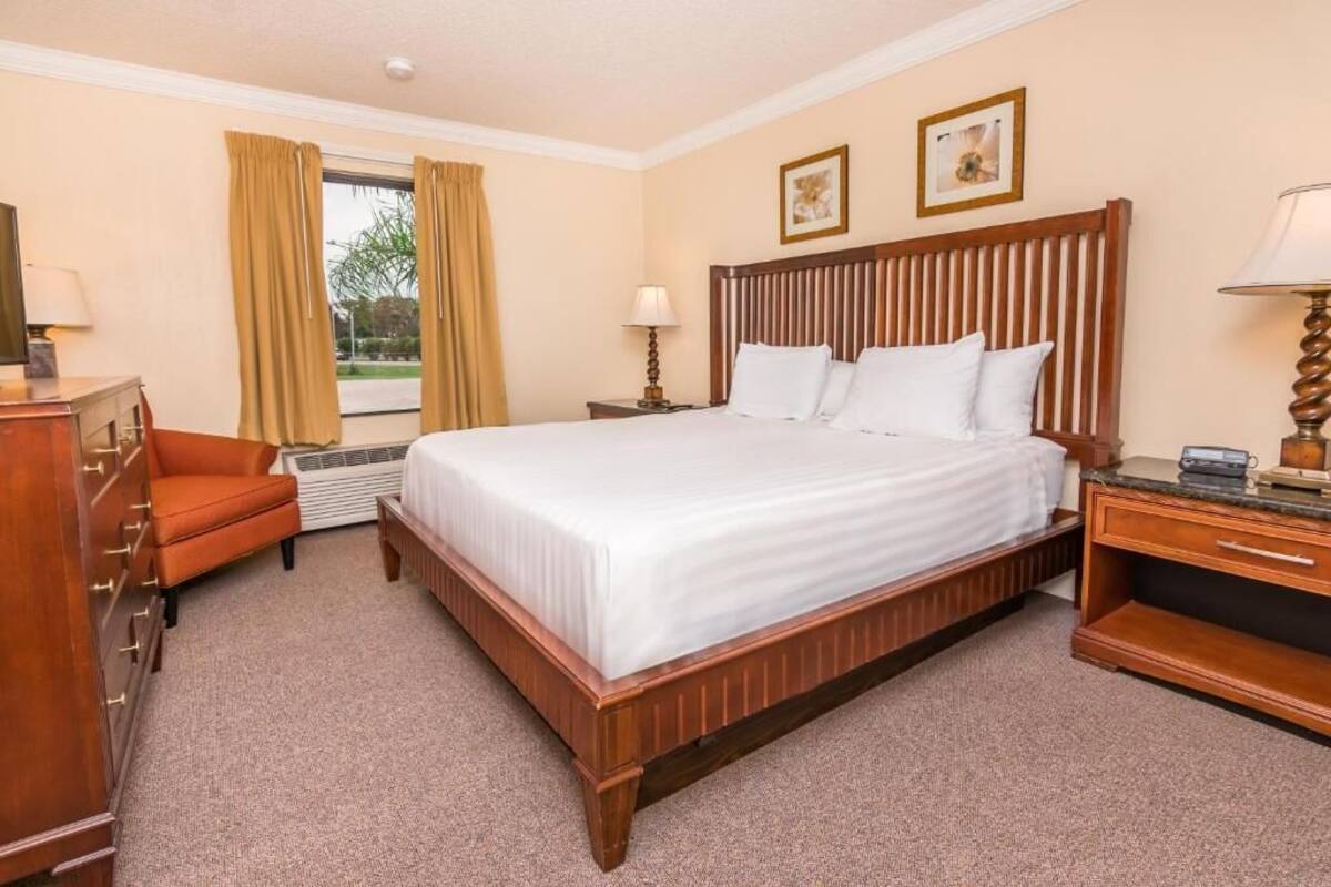 A hotel room with a large bed, a wooden dresser, a chair, and a desk with a lamp.