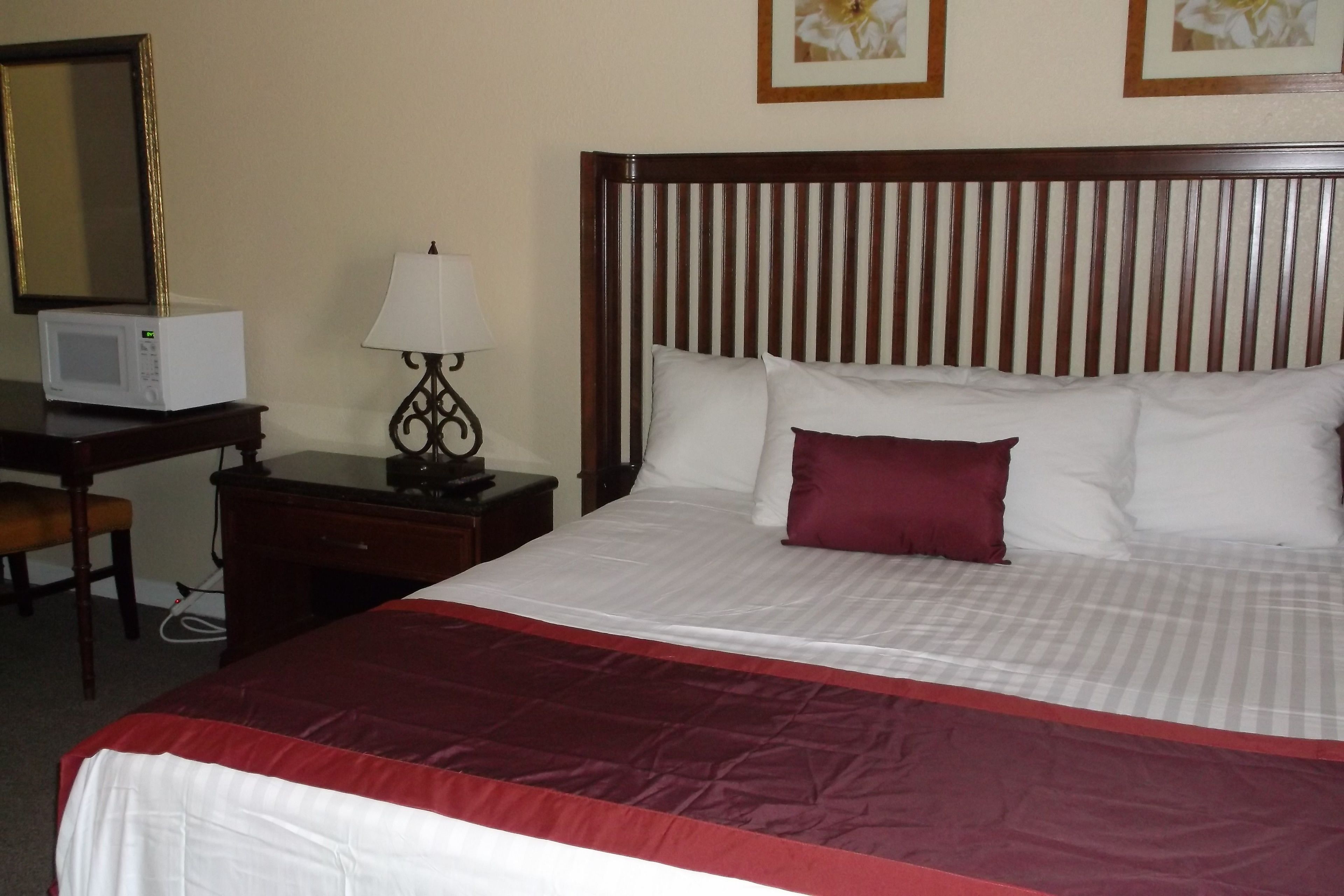 Una cama bien hecha con una colcha roja y blanca, un cabecero de madera y un almohadón blanco con detalles rojos.