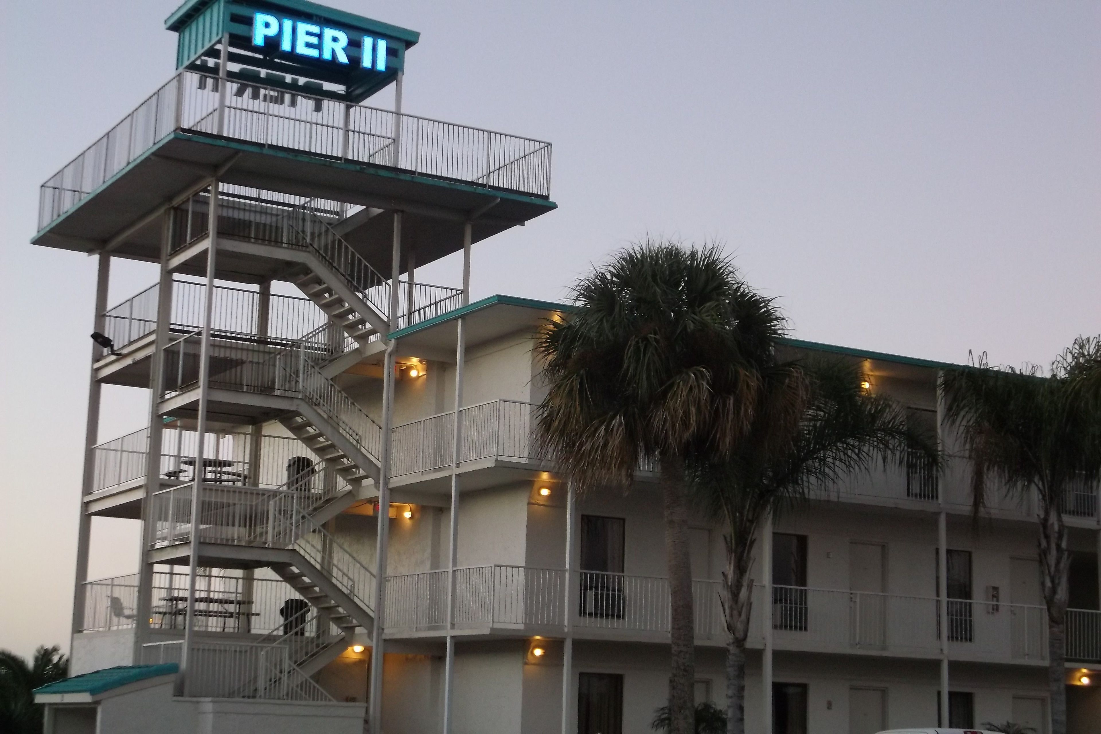 A multi-story hotel with a prominent "PIER II" sign, outdoor seating, and a palm tree.