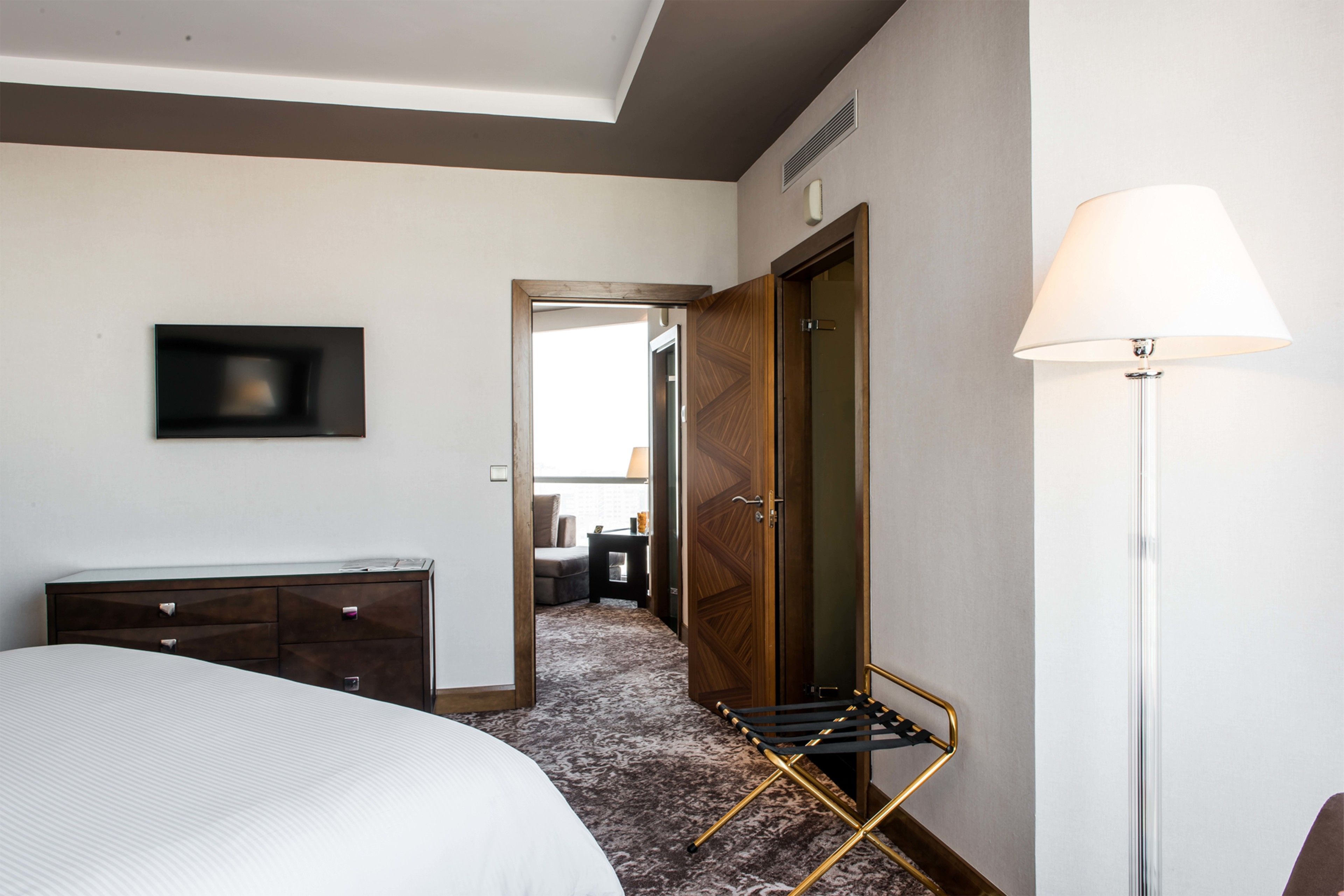 Quarto de hotel com cama, penteadeira, televisão na parede, abajur e guarda-roupa.