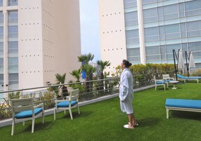 Un área de piscina en la azotea con sillones y una persona con bata.