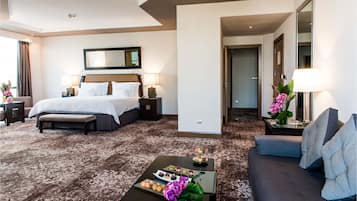 A hotel room with a large bed, a sitting area with a sofa, a coffee table with a tray of pastries, and a mirror above the bed.