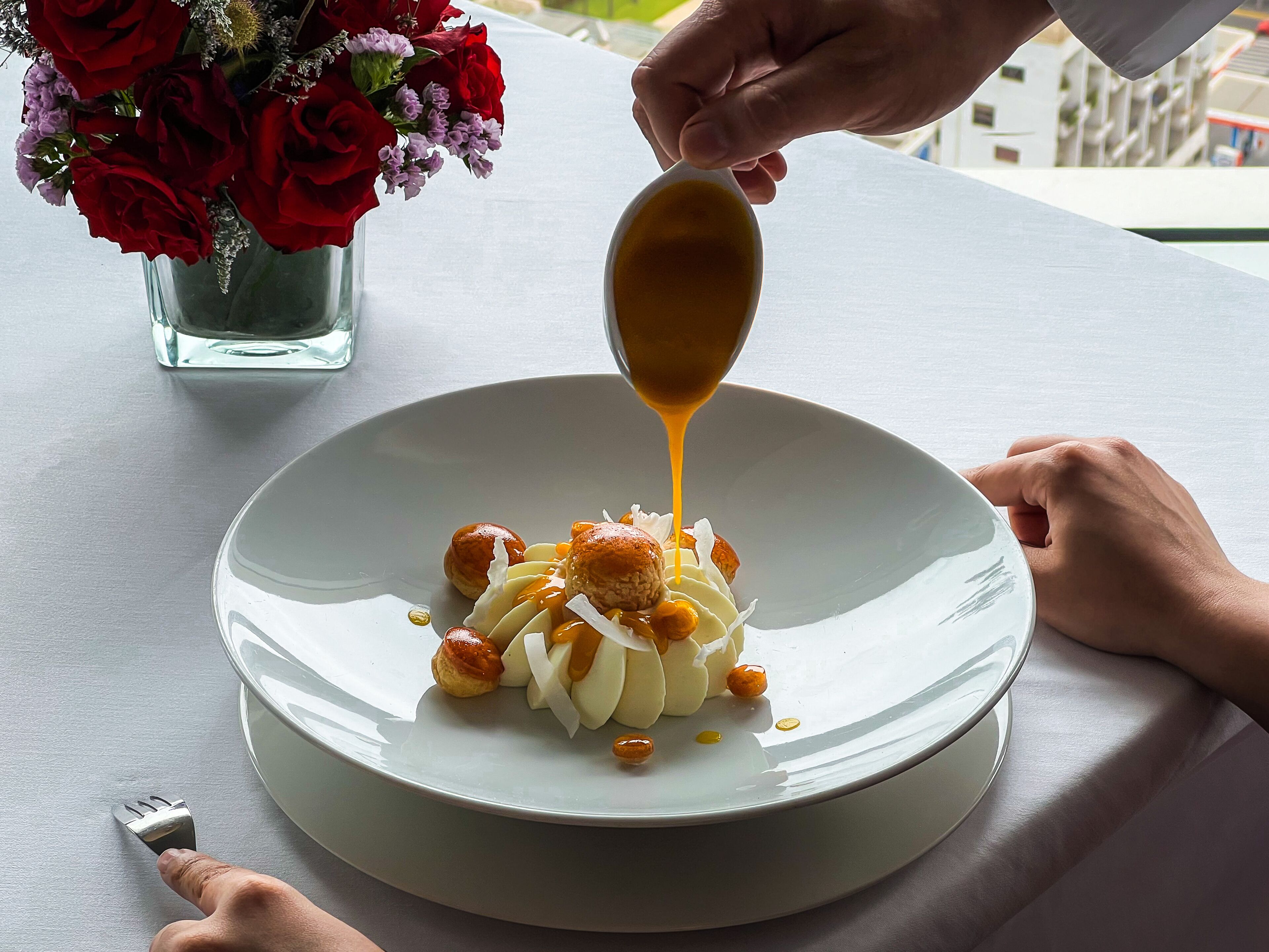 Une assiette de nourriture recouverte de sauce, une fourchette et une main tenant une cuillère.