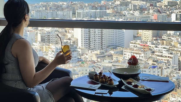 Una persona sentada a una mesa con vista a la ciudad y al mar.