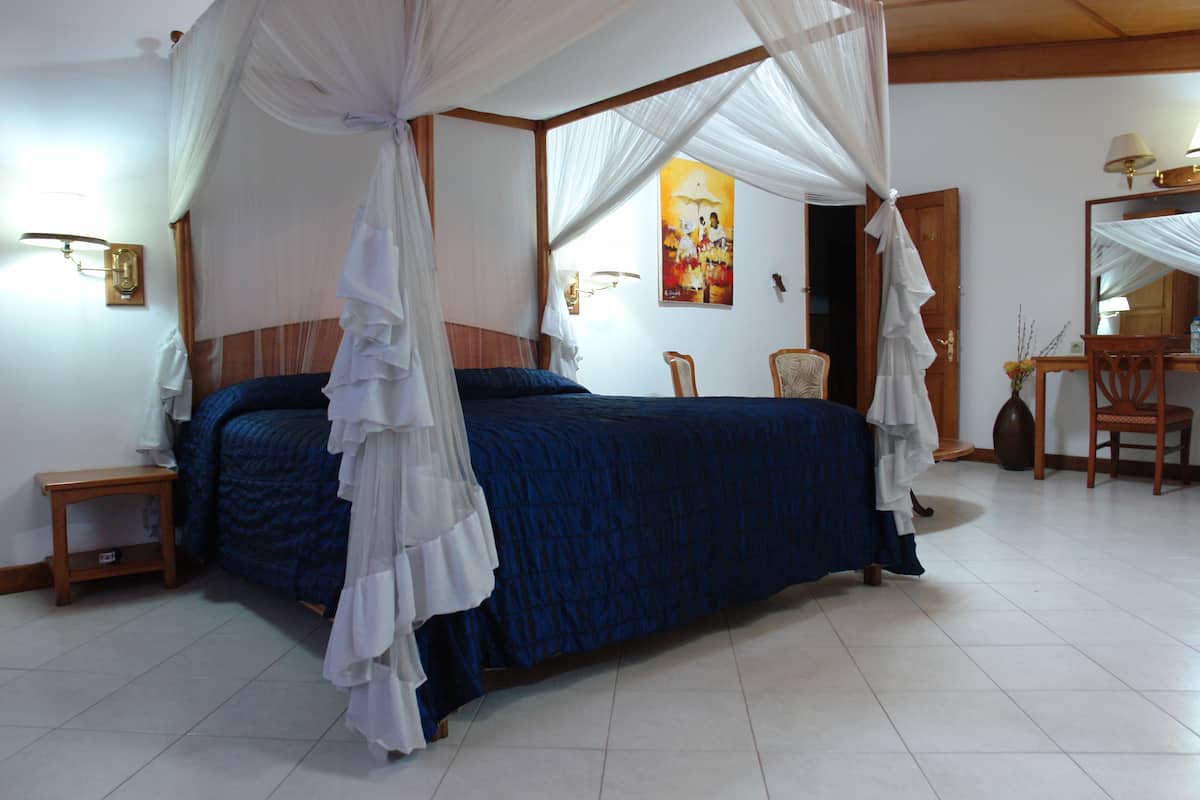 A bedroom with a canopy bed, a small bedside table, a chair, and a desk with a lamp.