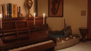 Un piano con un banco, un florero y libros en una estantería.