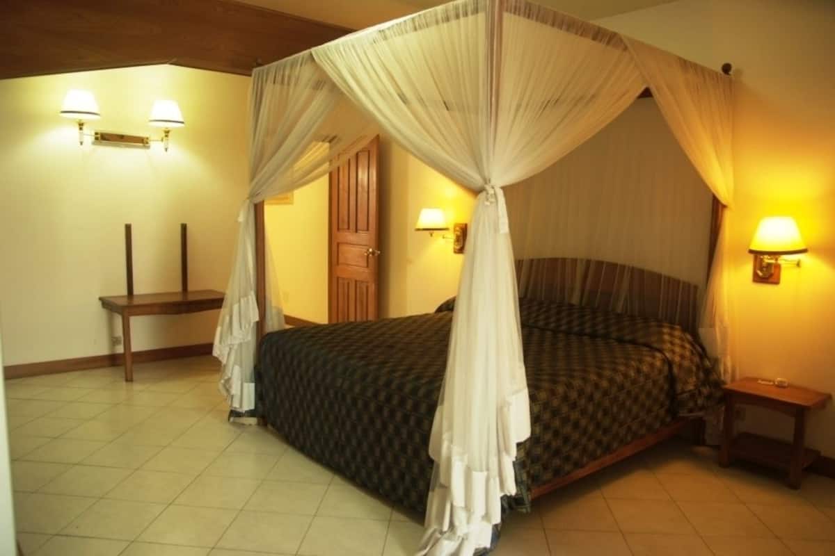 A four-poster canopy bed with a checkered bedspread, two bedside lamps, and a wooden nightstand.