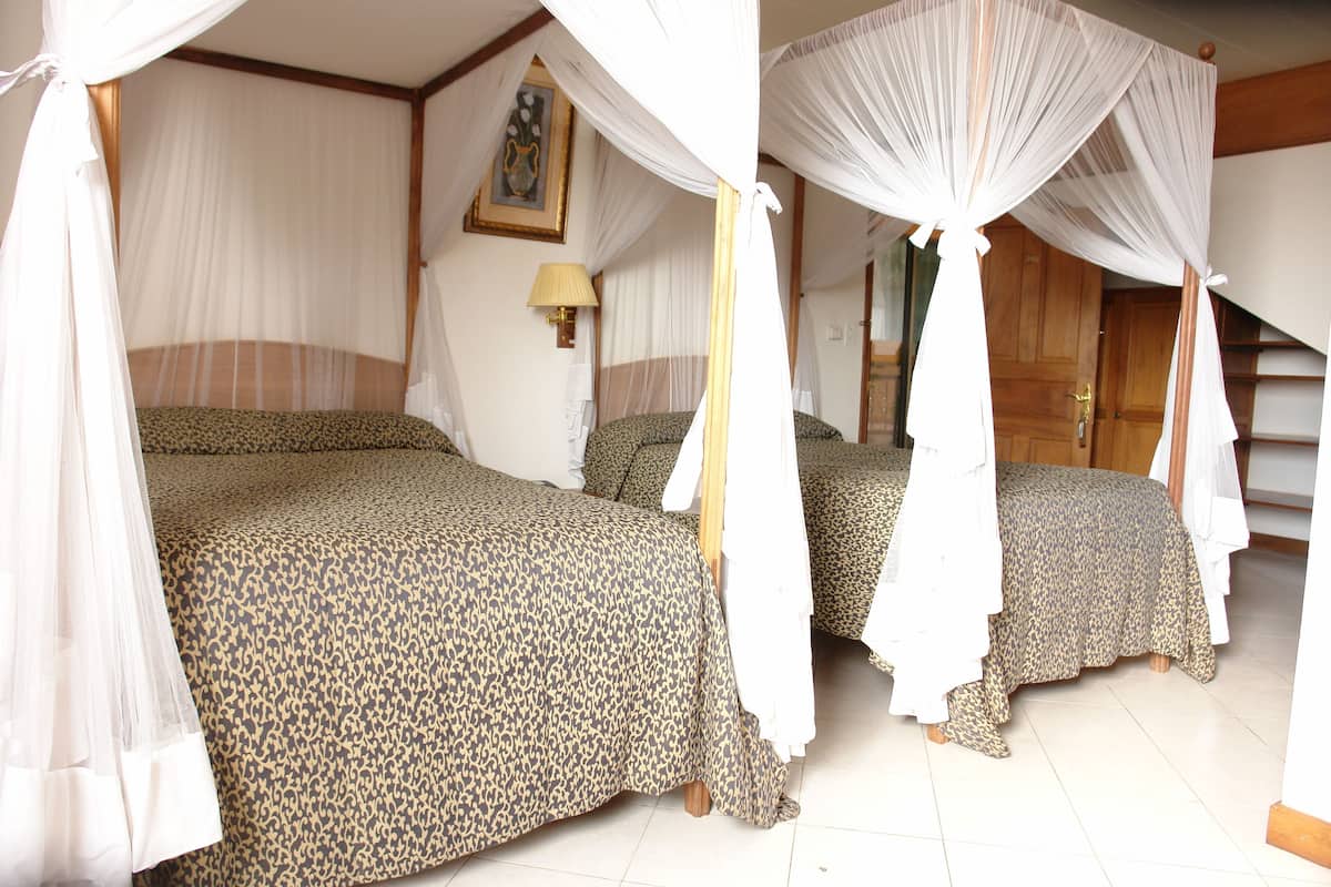 A room with two beds, each with a canopy bedspread and a nightstand with a lamp.