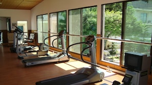 Un gimnasio con cintas de correr y equipo de ejercicio, amplias ventanas que ofrecen vistas a zonas verdes.