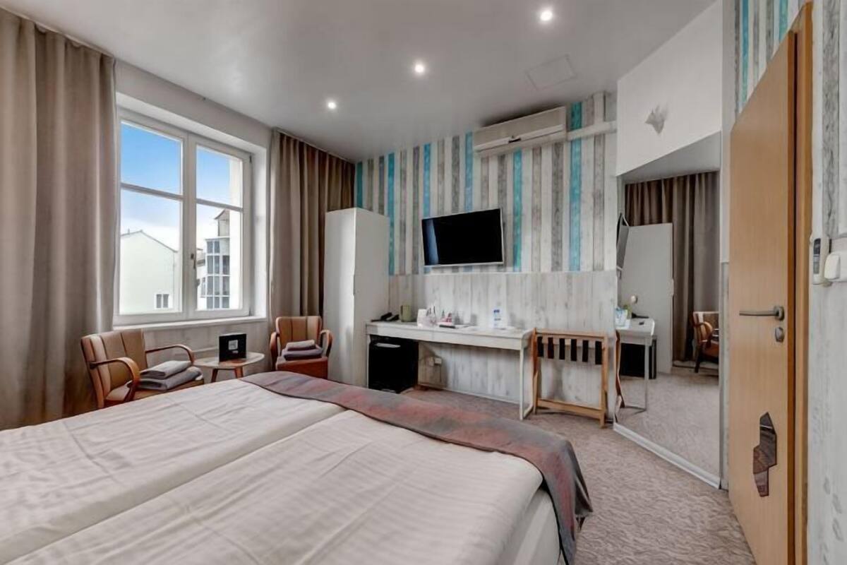 A hotel room with a bed, desk, chairs, a TV, and a view of the outside.
