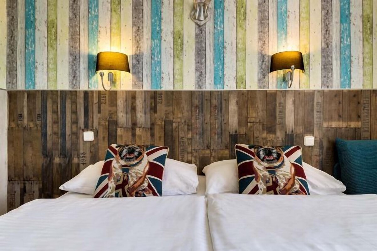 A hotel room with a wooden headboard, two wall-mounted lamps, and pillows with a Union Jack design.