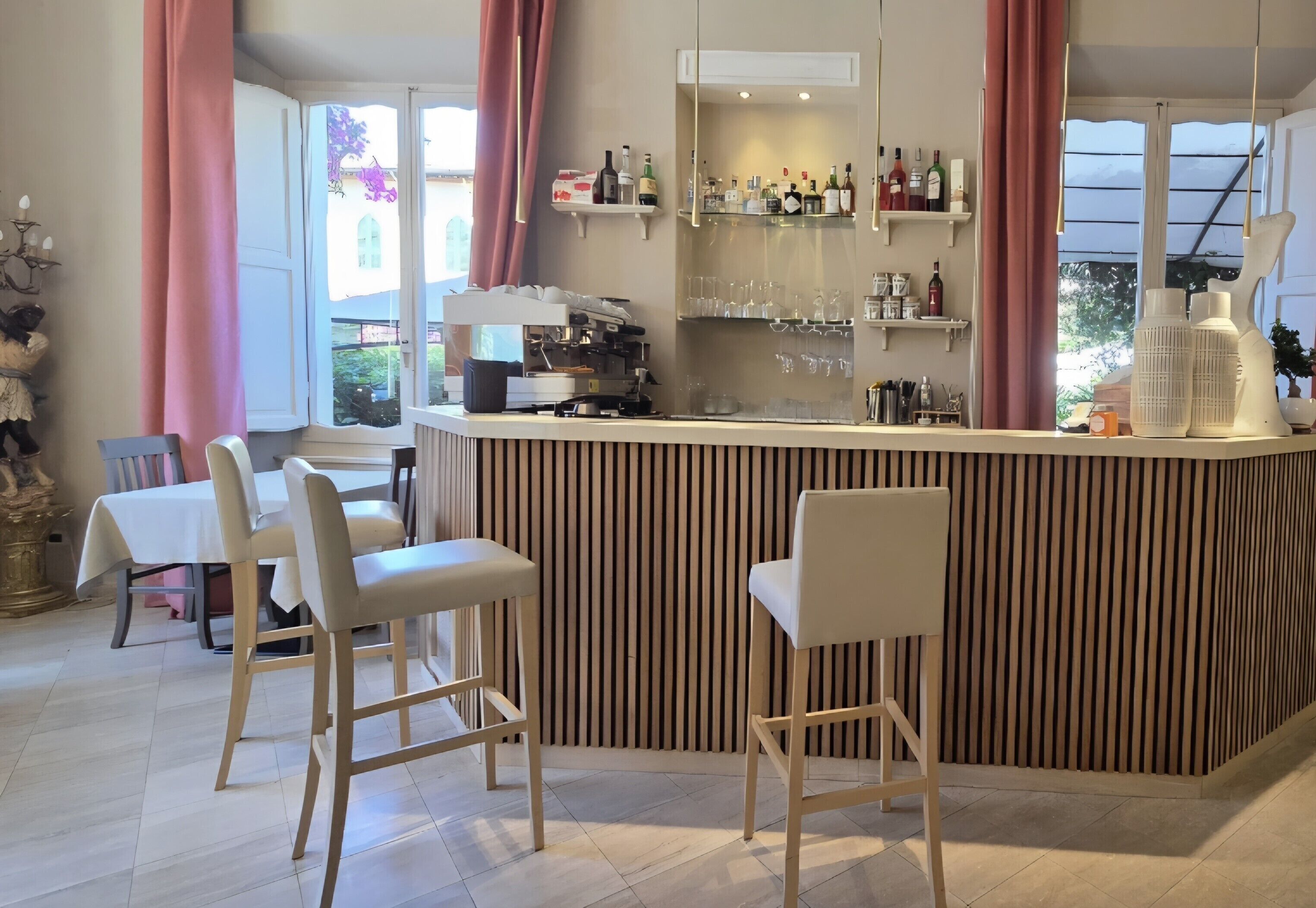 Uma área de bar com banquetas, balcão com garrafas e vista para o exterior.