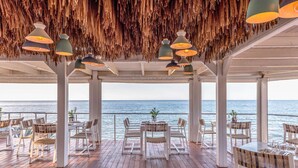 An outdoor dining area with wooden flooring, white chairs, and tables, overlooking the sea. - Ikaros Beach Resort & Spa - Adults Only (Hersonissos)