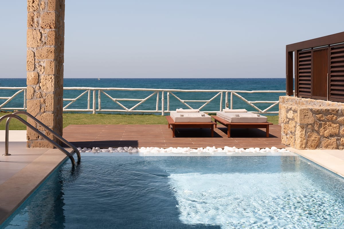 Piscina infinita com espreguiçadeiras, um pilar de pedra e vista para o oceano.