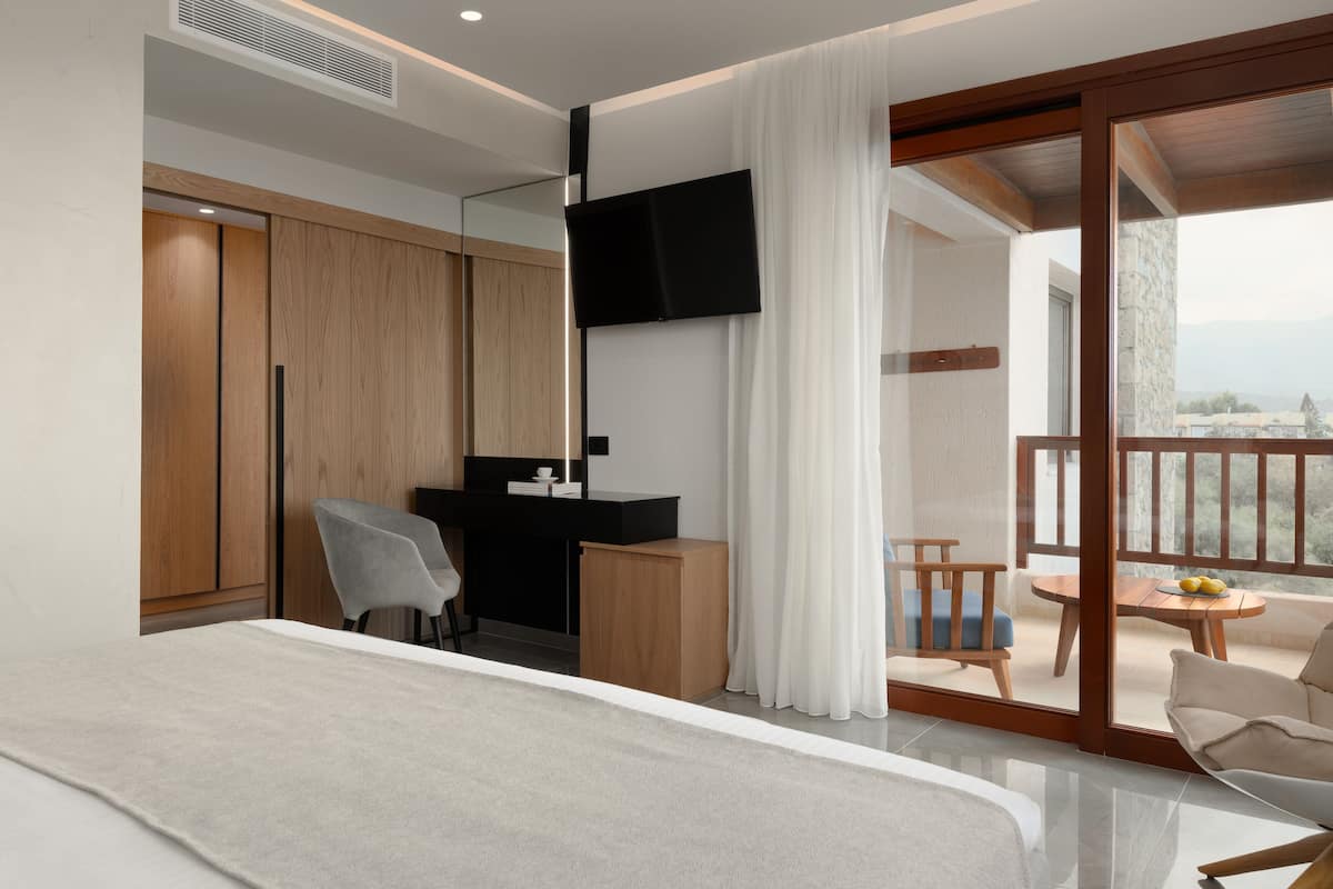 Quarto de hotel moderno com cama, escrivaninha, cadeira, televisão e varanda com mesa e cadeiras.