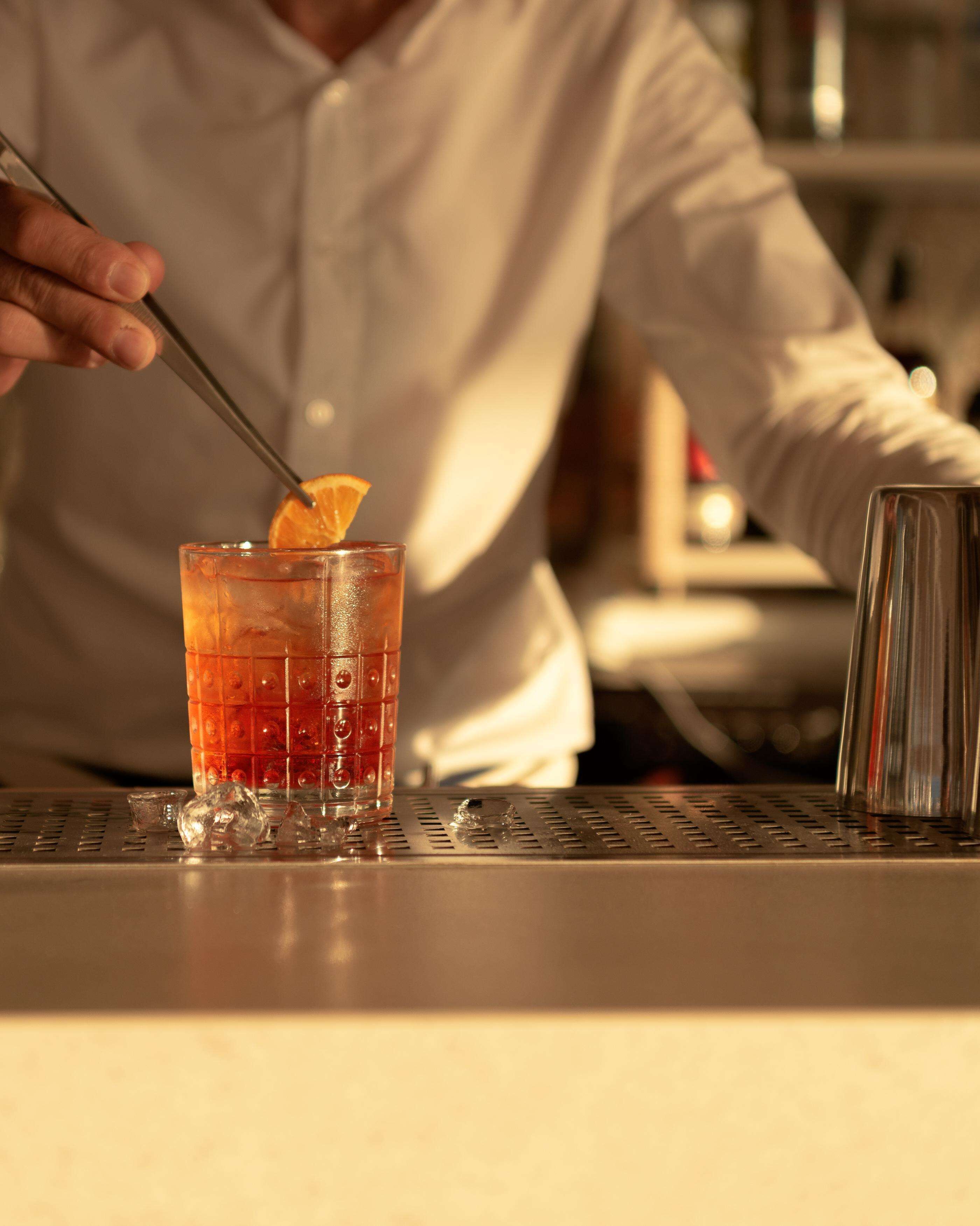 En bartender som blandar en drink med hjälp av en shaker och ett glas vid bardisken.