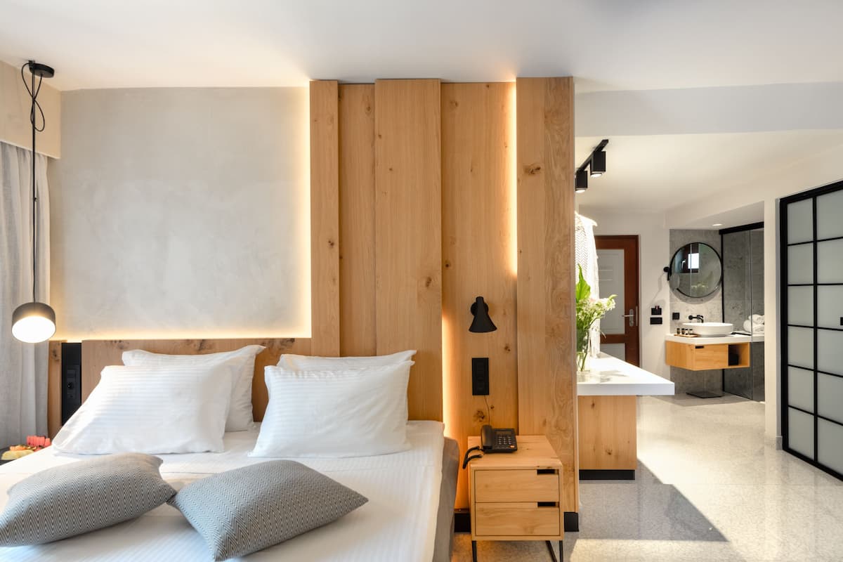 Quarto de hotel moderno com uma cama grande, mesa de cabeceira e um espaço de banheiro compacto.
