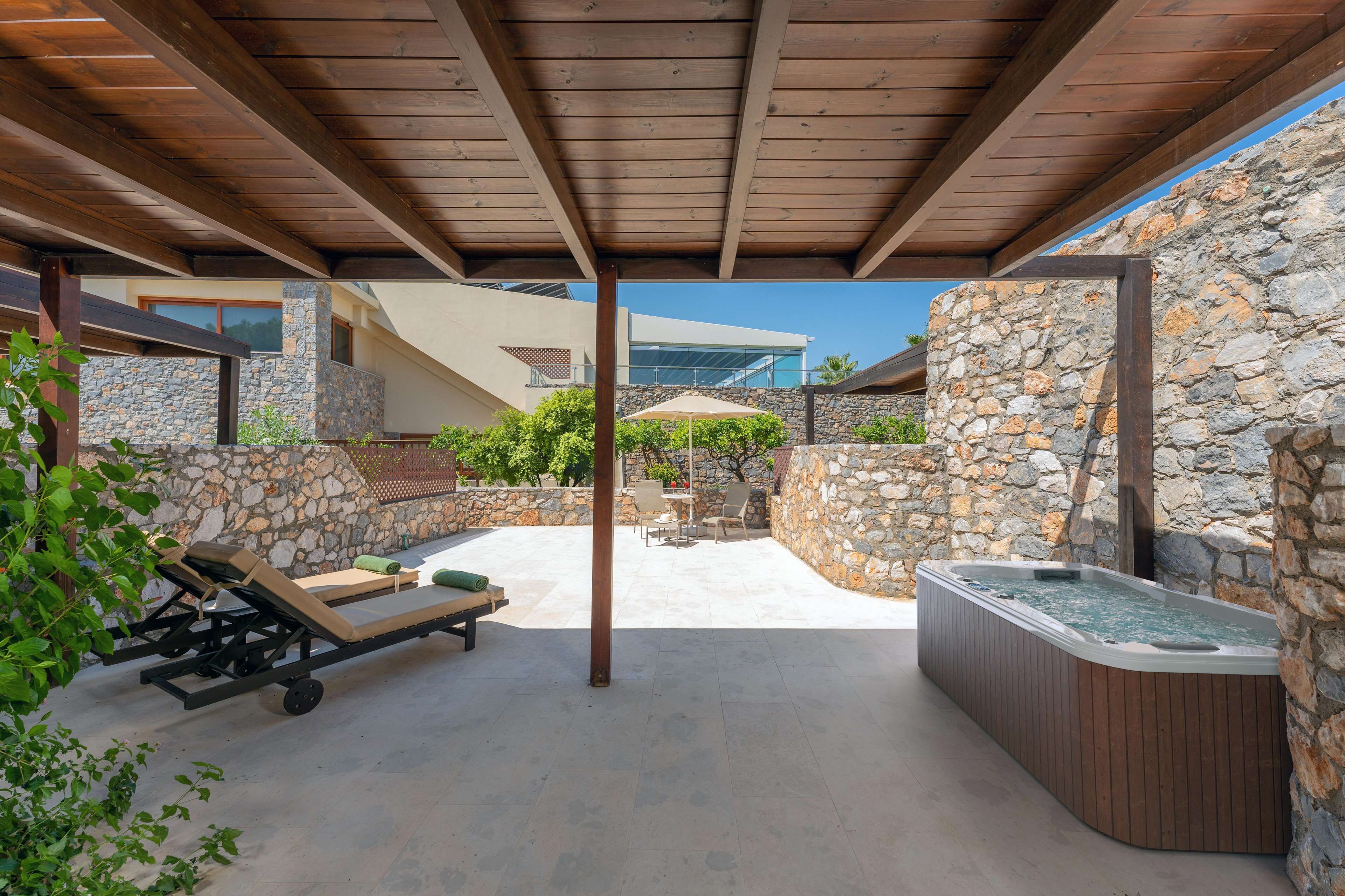 A covered outdoor area with a hot tub, lounge chairs, and stone walls.