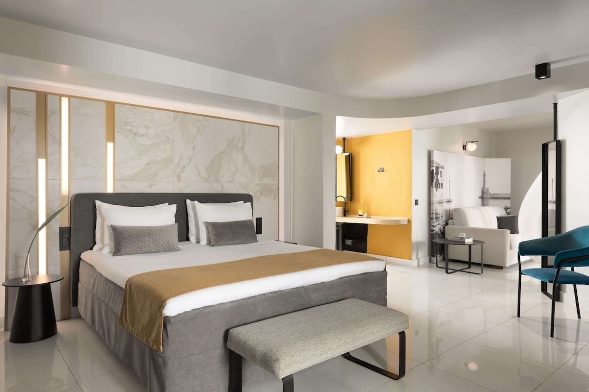 Quarto de hotel moderno com uma cama grande, um banco, uma escrivaninha e uma cadeira.