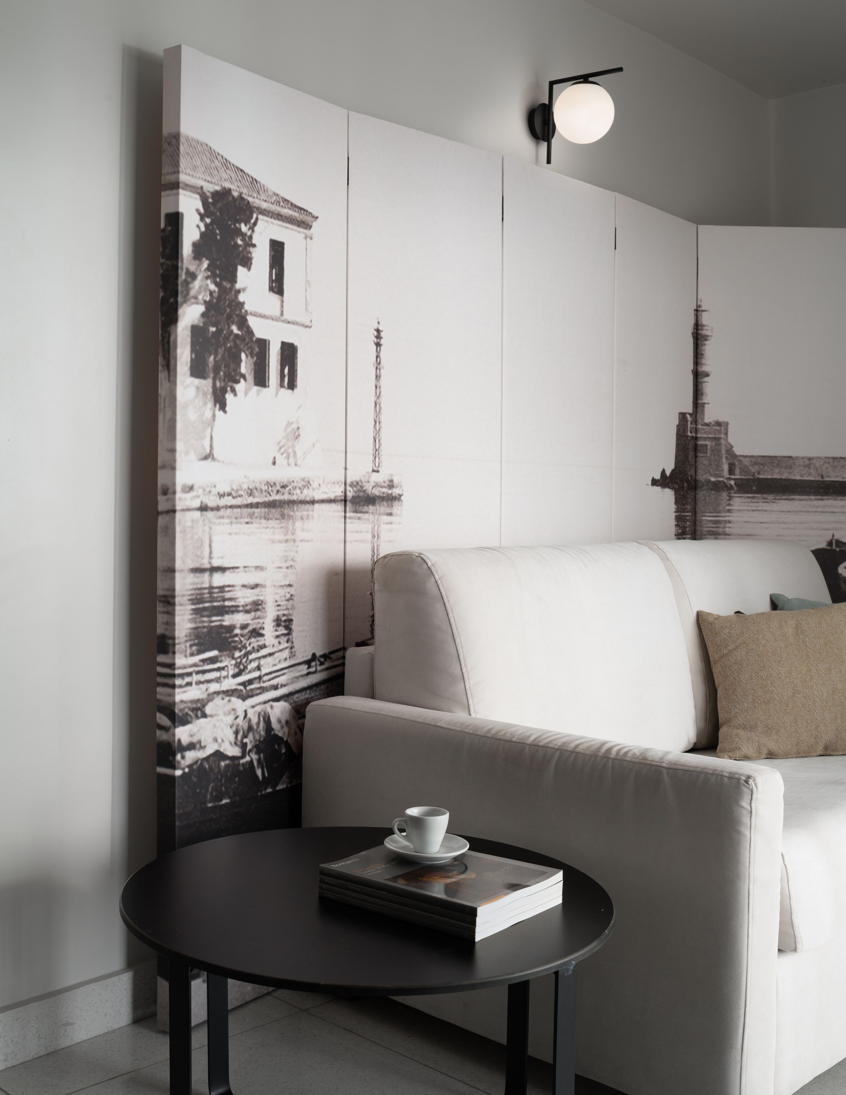 A modern living room with a sofa, a coffee table with a book and a cup, and a wall with large black-and-white photographs.