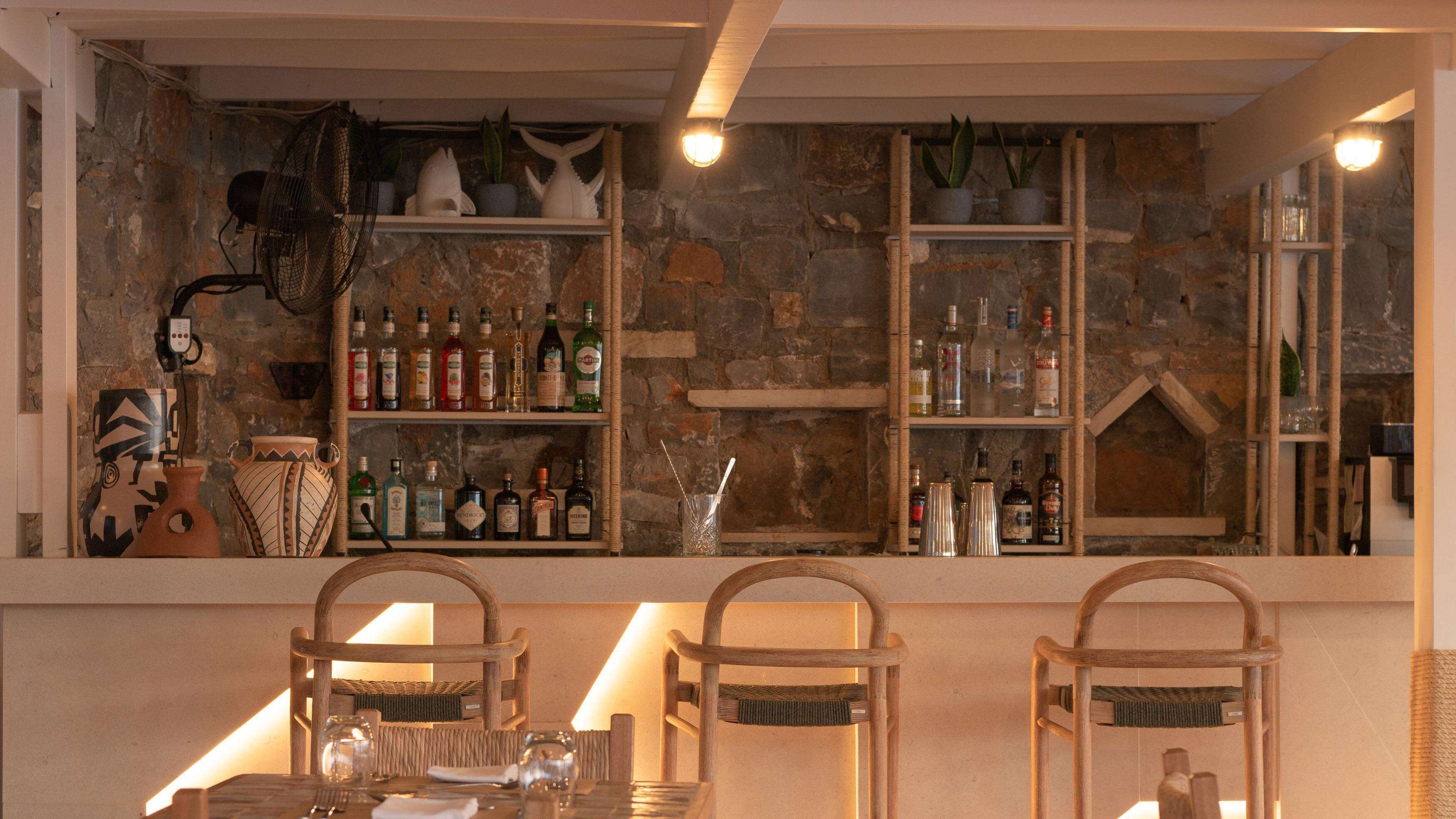A bar area with wooden shelves displaying various bottles, a fan, and decorative items.