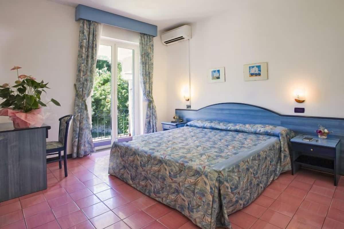 Une chambre à coucher comprenant un lit, un bureau, une chaise, une fenêtre avec des rideaux et un climatiseur fixé au mur.