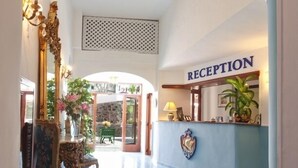 A reception area with a sign labeled "RECEPTION," a reception desk, a decorative mirror, and a chair with floral upholstery.