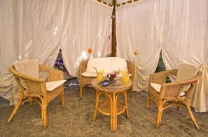Ein Zimmer mit Korbmöbeln, einem runden Tisch mit Getränken und transparenten Vorhängen.