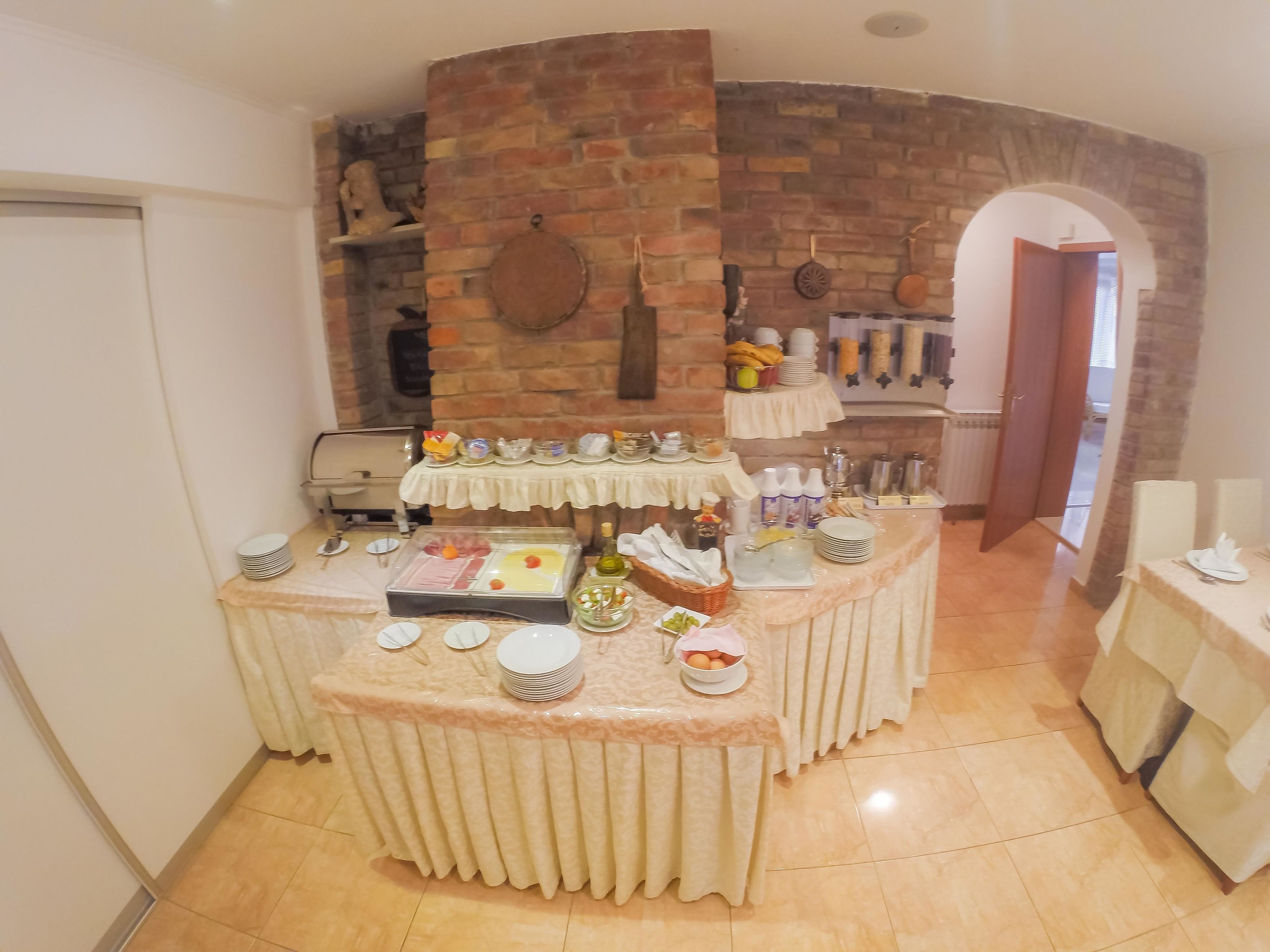A buffet setup with various food items and utensils, a brick wall, and a door leading to another room.