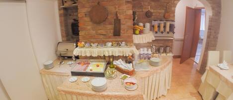 A buffet setup with various food items and utensils, a brick wall, and a door leading to another room.