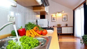 A kitchen with a sink, faucet, and various vegetables like lettuce, carrots, and tomatoes. There is a microwave and a cabinet in the background.