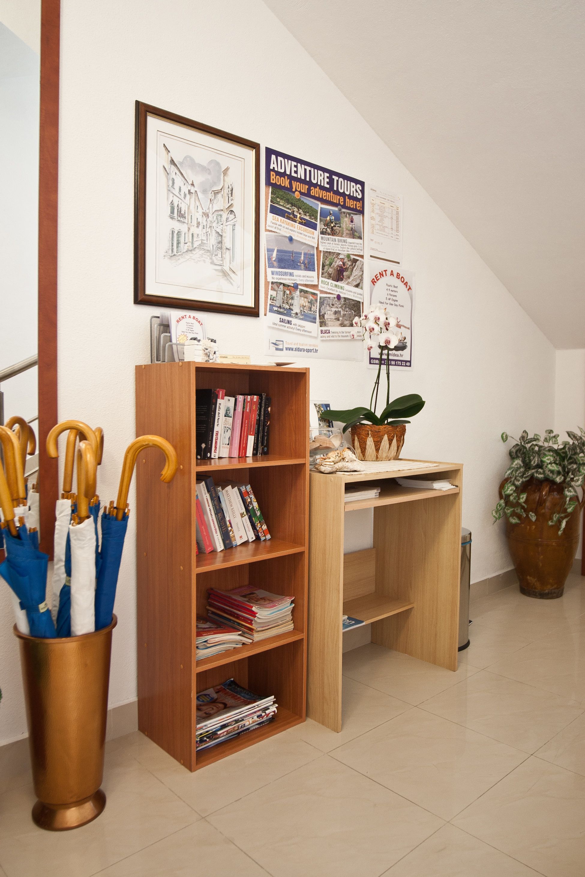 A room with a wooden bookshelf, a desk, a potted plant, and a brass container holding umbrellas.