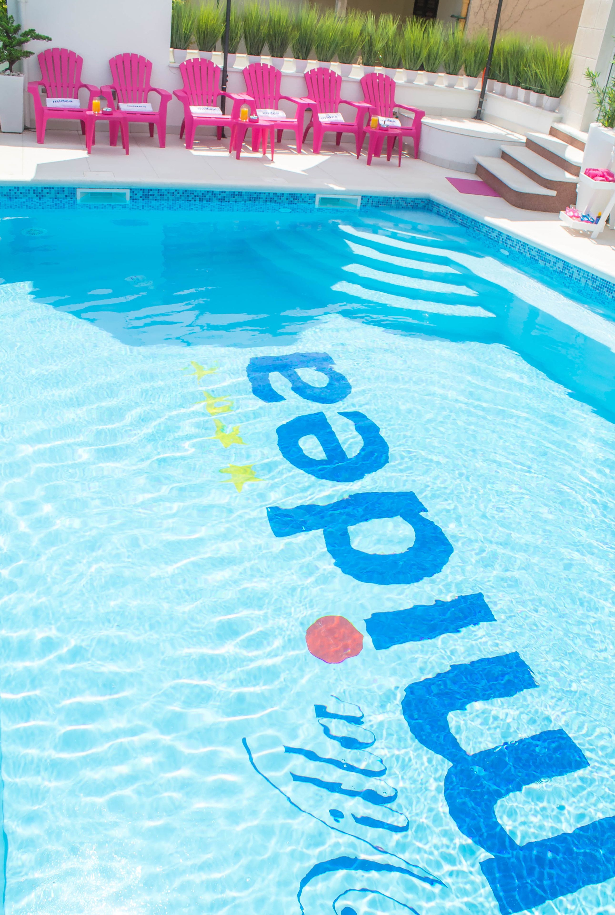 A swimming pool with a blue and white tiled edge, surrounded by pink chairs and a white wall.